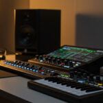 Modern home recording studio setup with professional audio equipment on a clean wooden desk. A Focusrite audio interface, KRK studio monitors, and MIDI controller are arranged elegantly under warm ambient lighting.
